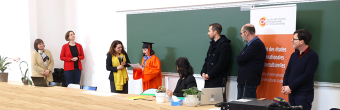 Des enseignantes et des enseignants sont rassemblés sur l'estrade l'aphithéâtre pour remettre son diplôme à une étudiante.