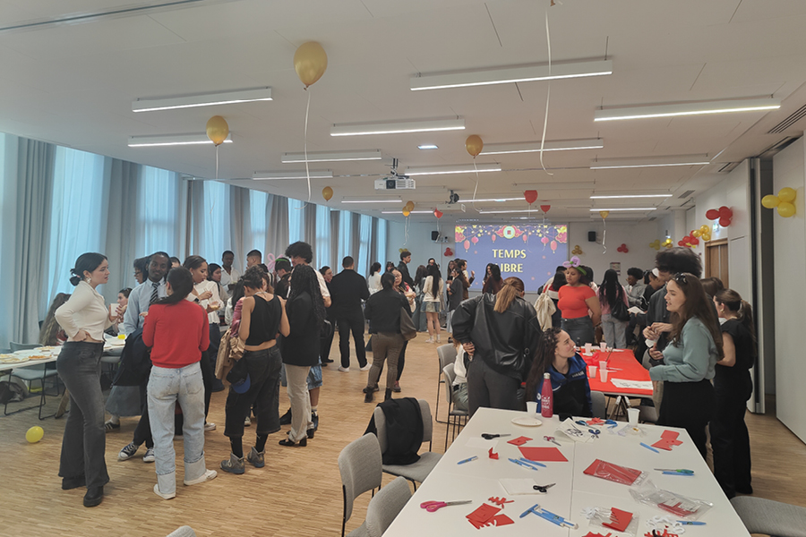 La salle est animée par de nombreuses conversation entre les personnes présentes. Au plafond, des ballons rouges et dorés ont été gonflés pour une ambiance festive