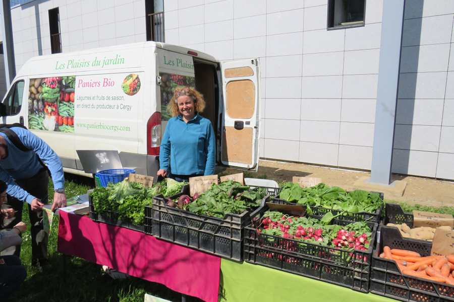 Une dame pose en souriant devant un étale des fruits et légumes bio