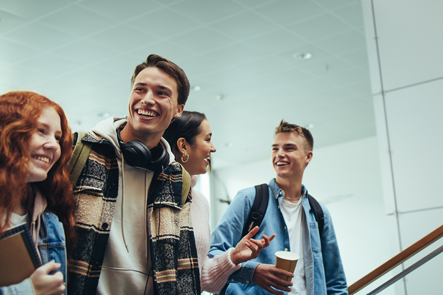 Un groupe de jeunes étudiantes et étudiants marchent dans les couloirs en souriant, un café à la main