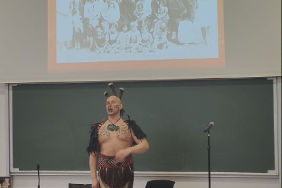 un homme habillé en costume traditionnel Maori fait une présentation dans un amphithéâtre